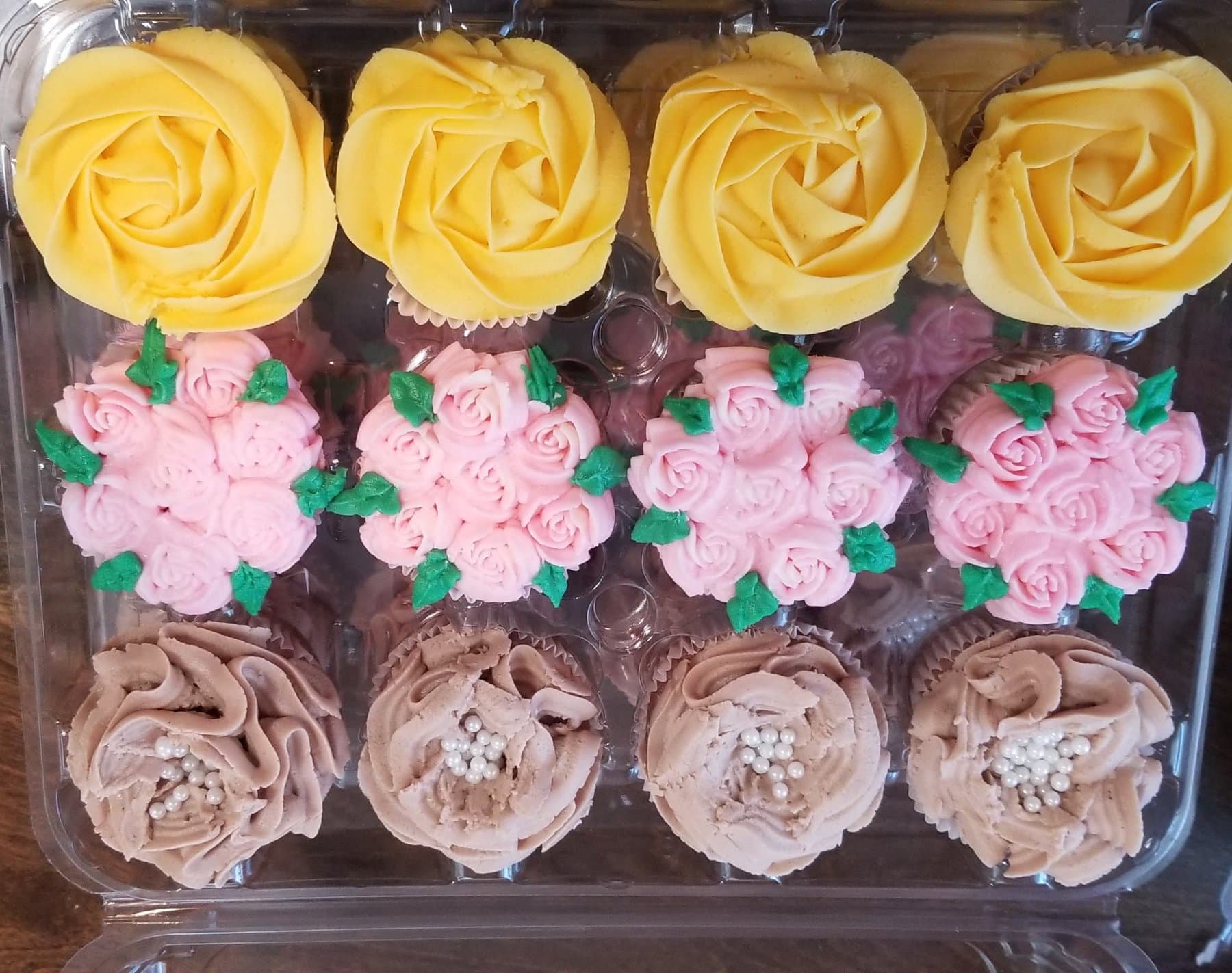 Assorted custom cupcakes with yellow rosettes, pink flowers, and chocolate buttercream by Jamie Cakes.