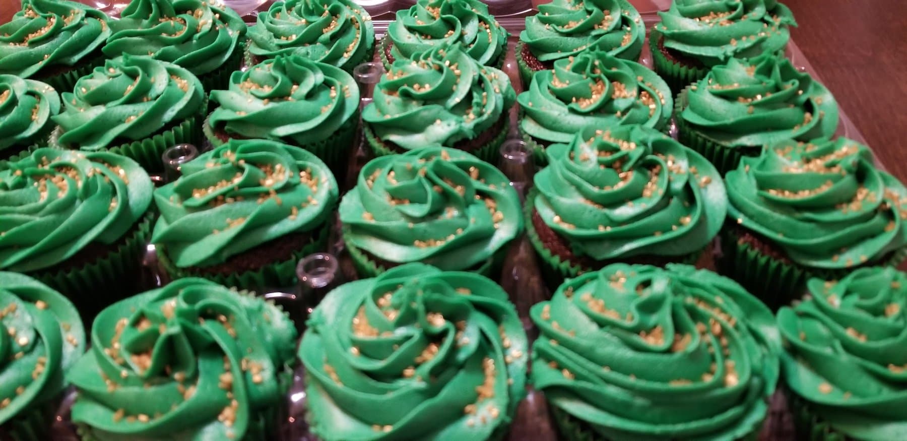 Green buttercream cupcakes with gold sprinkles and dark chocolate centers by Jamie Cakes.