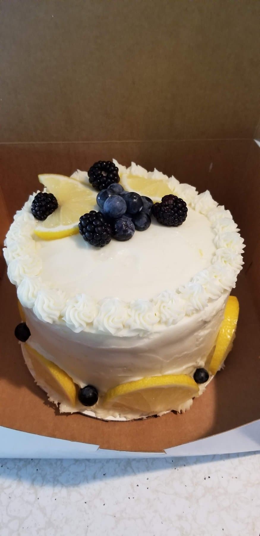 White buttercream cake with fresh berries, lemon slices, and a gold accent band by Jamie Cakes.