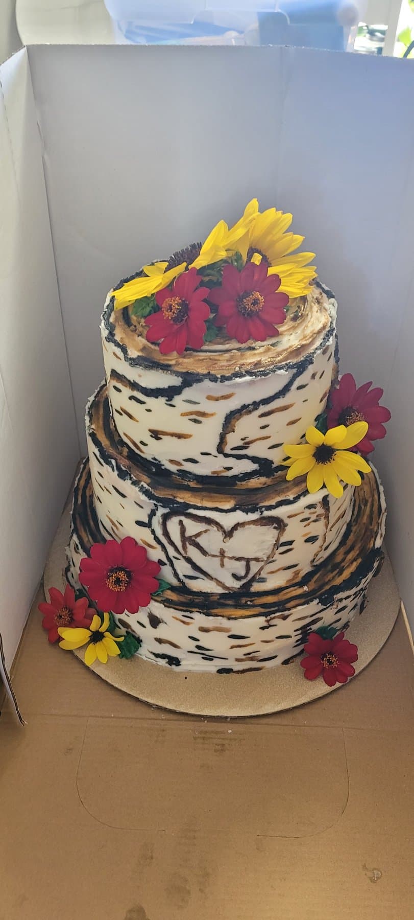 Rustic tiered cake with sunflower accents and bark-style buttercream texture by Jamie Cakes.